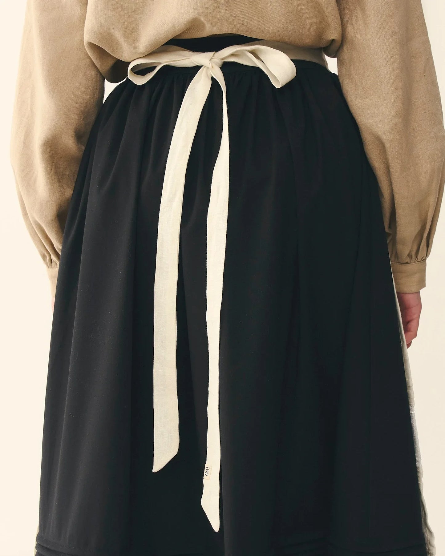 Traditional Ukrainian black skirt with beige blouse, apron tie at waist, back view