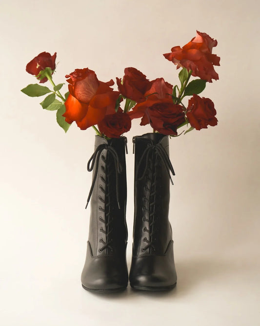 Black lace-up Victorian boots with red roses inside, minimalist background