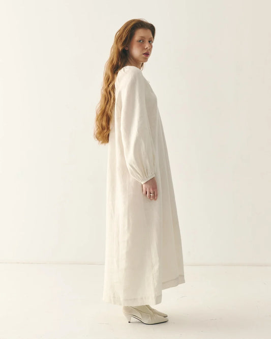 Woman in long, loose-fitting traditional white linen dress with puff sleeves, side view