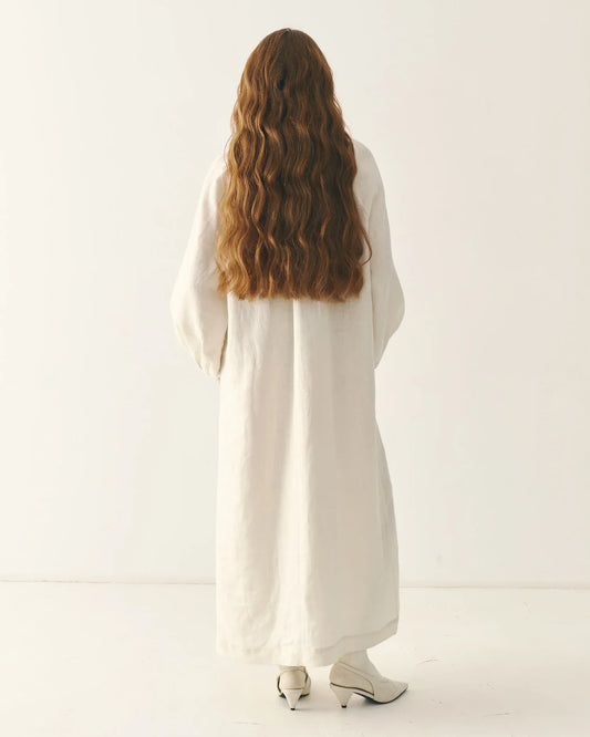 Woman in long white traditional Ukrainian dress with long wavy hair, standing indoors